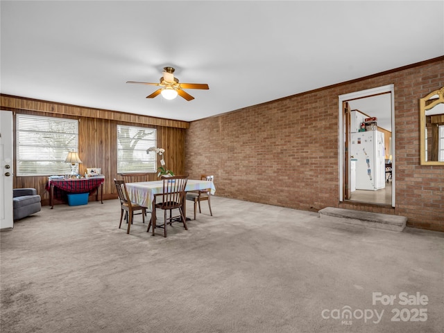 carpeted dining area featuring ceiling fan and brick wall