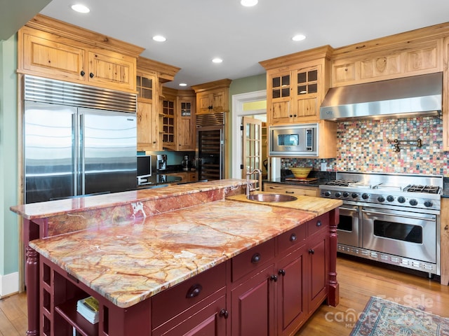 kitchen with sink, built in appliances, a kitchen island with sink, and ventilation hood