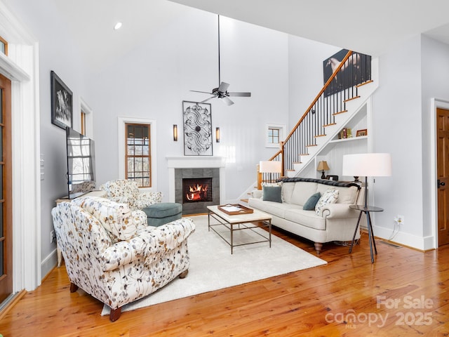 living room featuring a towering ceiling, a tile fireplace, ceiling fan, and hardwood / wood-style flooring