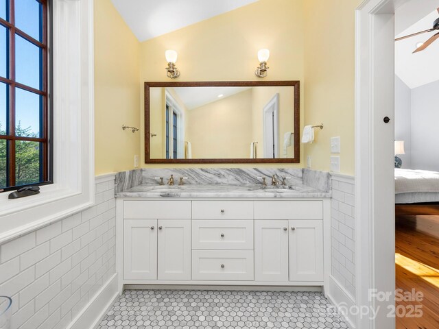 bathroom with tile patterned flooring, vaulted ceiling, vanity, ceiling fan, and tile walls