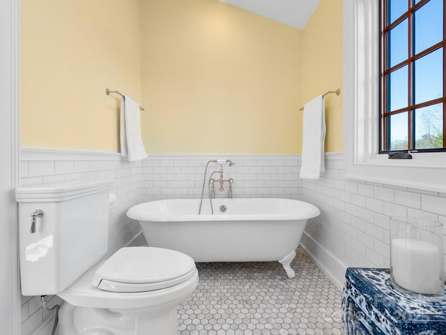 bathroom with toilet, tile patterned flooring, tile walls, and a bathtub