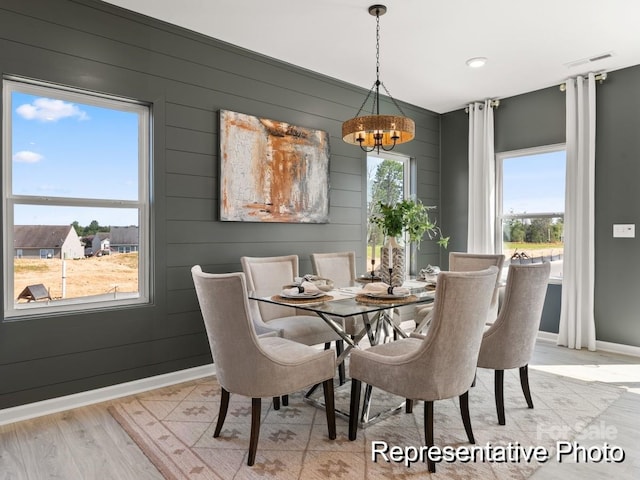 dining room featuring light wood-type flooring, plenty of natural light, a notable chandelier, and wood walls