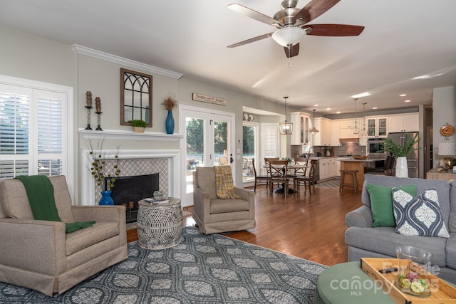 living room with a tiled fireplace, ceiling fan, plenty of natural light, and dark hardwood / wood-style floors