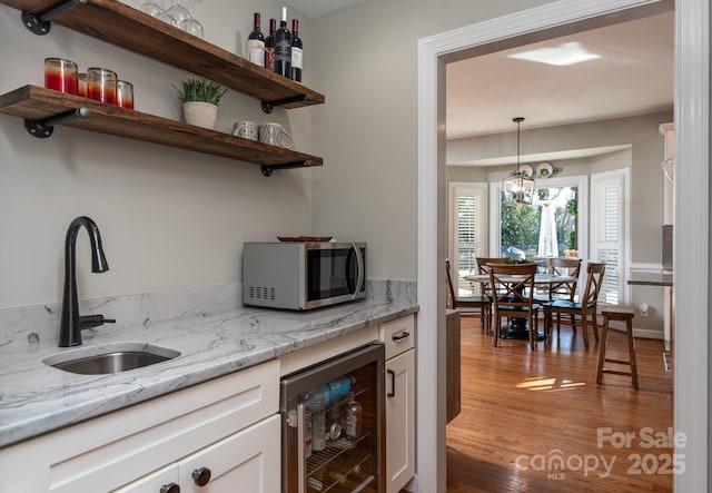 bar with wine cooler, light stone countertops, a notable chandelier, white cabinets, and sink