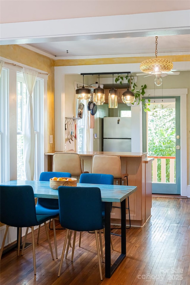 dining space featuring a healthy amount of sunlight, ornamental molding, and hardwood / wood-style flooring