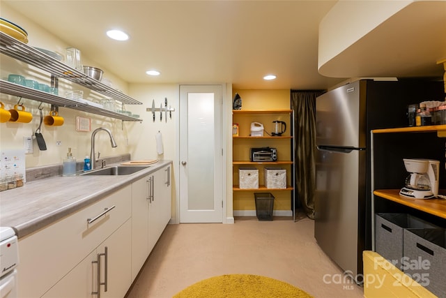 kitchen featuring sink, white cabinetry, and stainless steel refrigerator