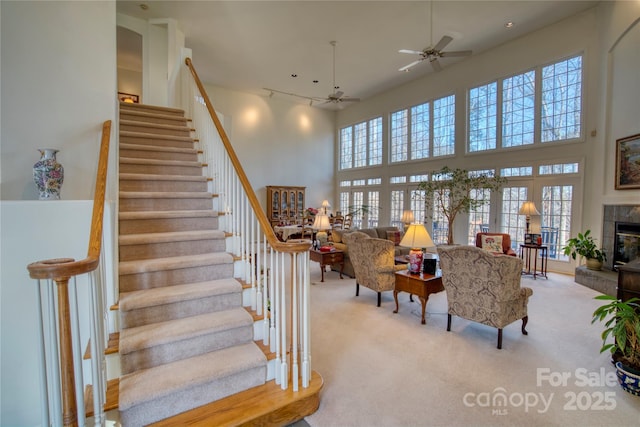 carpeted living room featuring ceiling fan, a fireplace, and a high ceiling