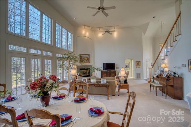 carpeted dining space featuring ceiling fan, a towering ceiling, and french doors