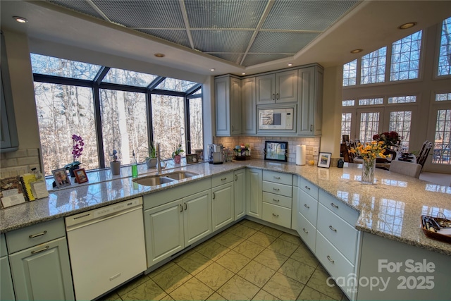 kitchen featuring kitchen peninsula, light stone counters, sink, and white appliances