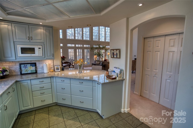 kitchen with light carpet, kitchen peninsula, backsplash, and light stone counters