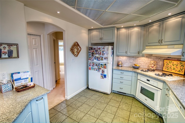 kitchen featuring decorative backsplash, light stone counters, white appliances, and gray cabinetry