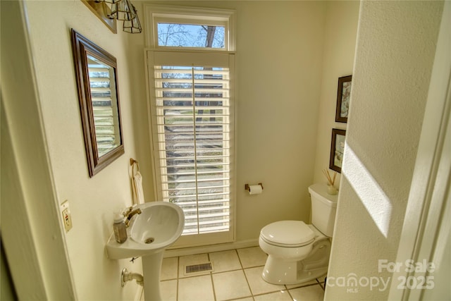 bathroom with toilet, a healthy amount of sunlight, and tile patterned flooring