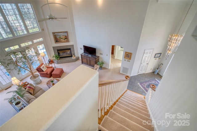 living room featuring a fireplace, a towering ceiling, and ceiling fan with notable chandelier