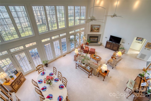 carpeted living room with french doors, ceiling fan, a tiled fireplace, and a high ceiling