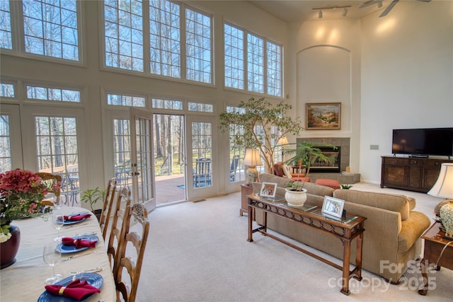 carpeted living room with a tiled fireplace, a wealth of natural light, and a high ceiling