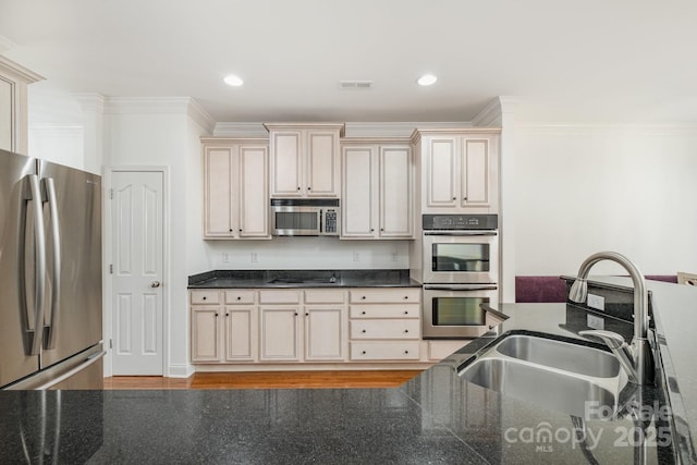 kitchen featuring appliances with stainless steel finishes, cream cabinets, dark stone counters, and sink