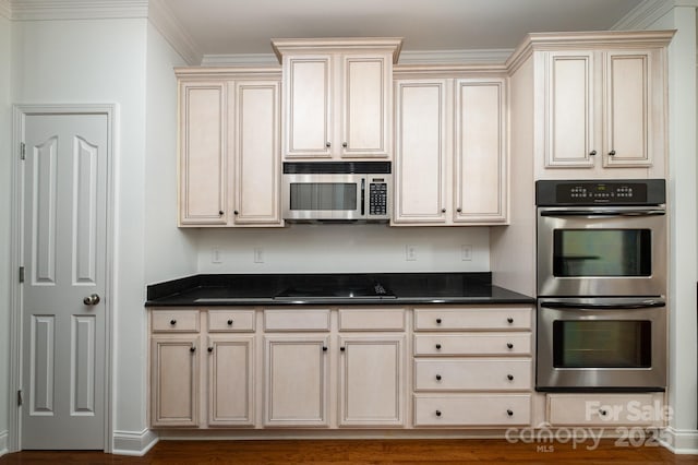 kitchen with cream cabinetry, appliances with stainless steel finishes, dark stone countertops, and crown molding