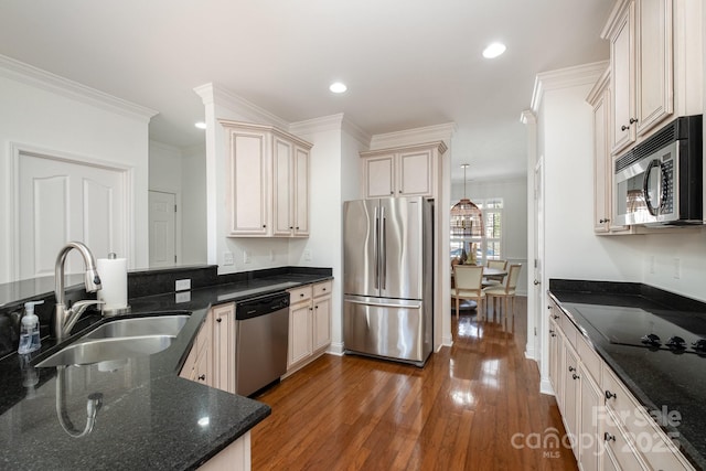 kitchen with stainless steel appliances, dark stone countertops, sink, hanging light fixtures, and crown molding