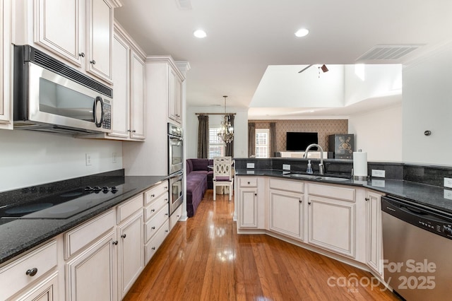 kitchen featuring stainless steel appliances, dark stone counters, hanging light fixtures, ceiling fan with notable chandelier, and sink