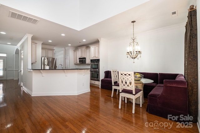 kitchen with white cabinets, decorative light fixtures, stainless steel appliances, kitchen peninsula, and a breakfast bar