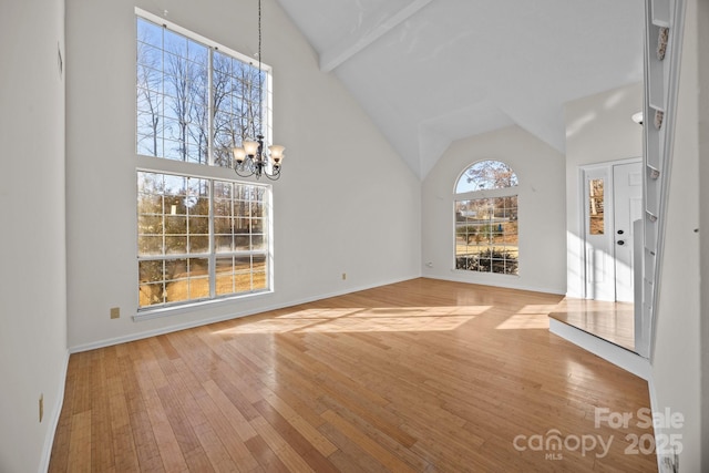 unfurnished living room featuring an inviting chandelier, hardwood / wood-style flooring, beamed ceiling, and high vaulted ceiling