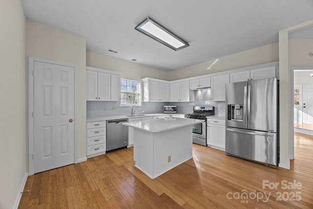 kitchen featuring decorative backsplash, white cabinets, a kitchen island, light hardwood / wood-style flooring, and stainless steel appliances