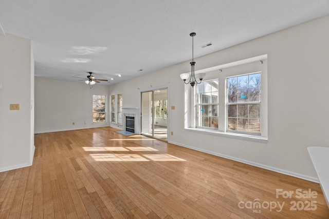 unfurnished living room with ceiling fan with notable chandelier, light hardwood / wood-style flooring, and a high end fireplace