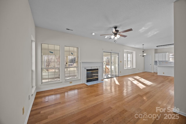 unfurnished living room with ceiling fan with notable chandelier, hardwood / wood-style flooring, a textured ceiling, and a premium fireplace