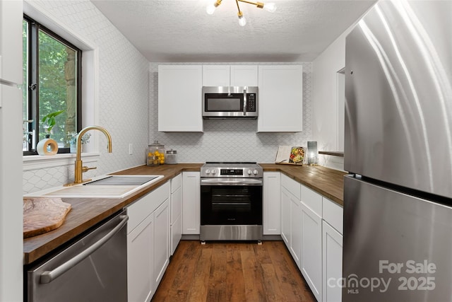 kitchen featuring appliances with stainless steel finishes, butcher block countertops, white cabinetry, and sink