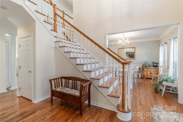 staircase featuring hardwood / wood-style flooring, ornamental molding, and a chandelier