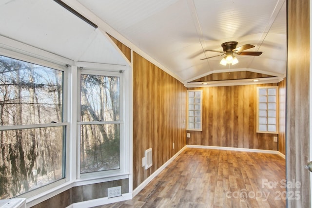 empty room with lofted ceiling, hardwood / wood-style flooring, ceiling fan, and wooden walls