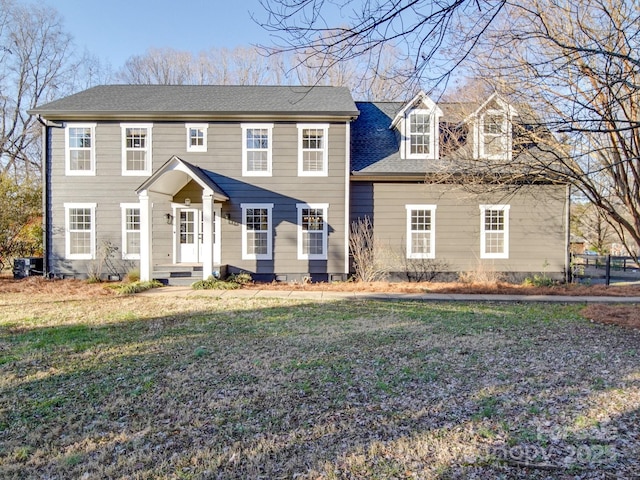 colonial house featuring a front lawn and roof with shingles