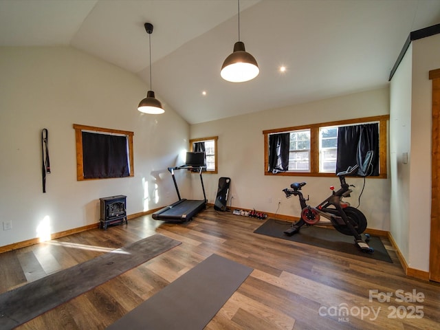 workout room featuring lofted ceiling, a wealth of natural light, a wood stove, and wood finished floors