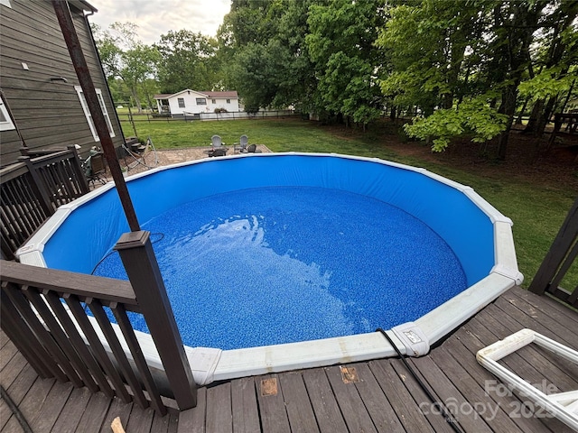 outdoor pool featuring a lawn, a deck, and fence