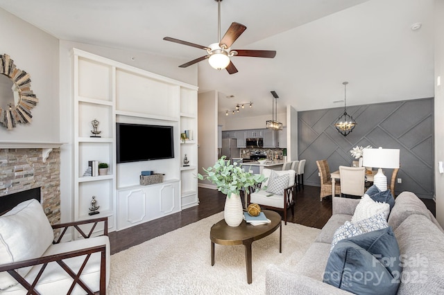 living area with a fireplace, vaulted ceiling, dark wood-type flooring, and ceiling fan with notable chandelier