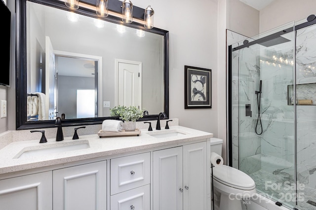 bathroom with toilet, double vanity, a marble finish shower, and a sink