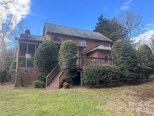 back of property with a wooden deck, a sunroom, and a lawn