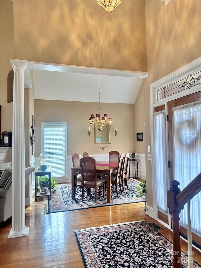 dining area featuring high vaulted ceiling, hardwood / wood-style flooring, an inviting chandelier, and ornate columns