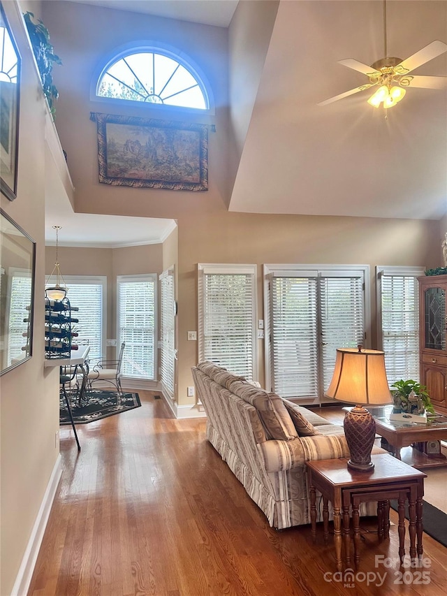 living room featuring ceiling fan, wood-type flooring, a wealth of natural light, and a towering ceiling