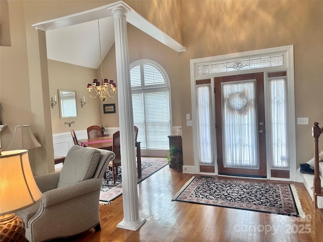 entryway with high vaulted ceiling, wood-type flooring, ornate columns, and a notable chandelier