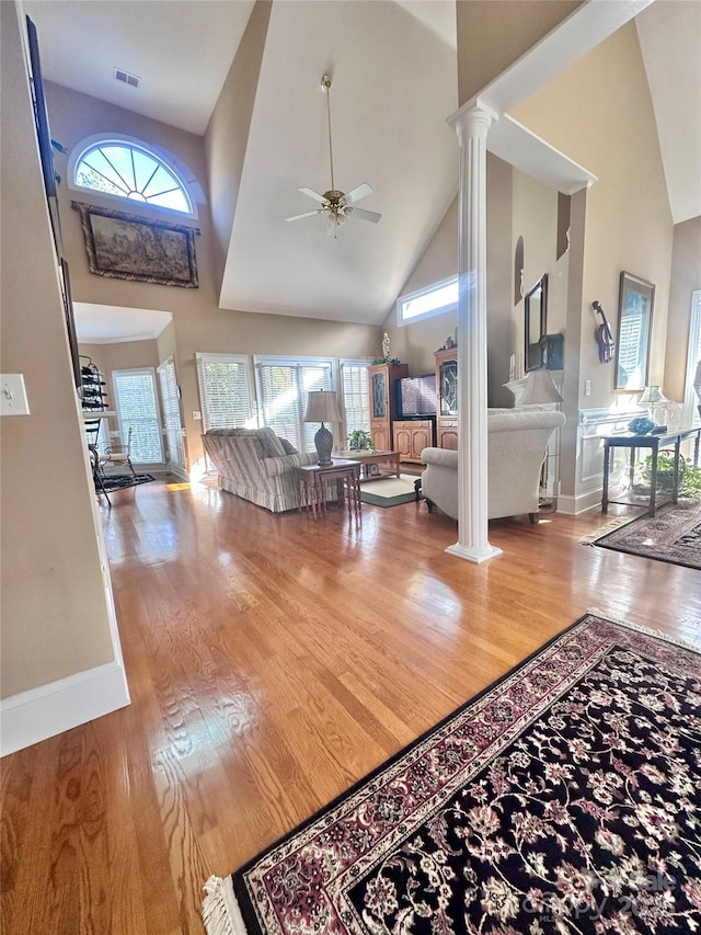 living room featuring ceiling fan, wood-type flooring, a high ceiling, and decorative columns