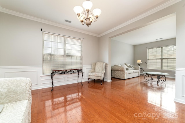 living area with a wealth of natural light, ornamental molding, wood-type flooring, and an inviting chandelier