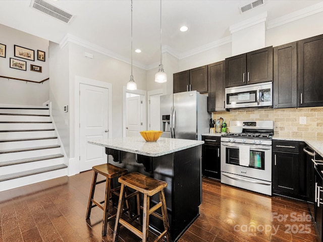 kitchen with a breakfast bar area, decorative light fixtures, a center island, stainless steel appliances, and light stone countertops