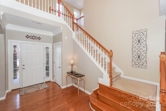 foyer entrance with a towering ceiling, hardwood / wood-style floors, and crown molding