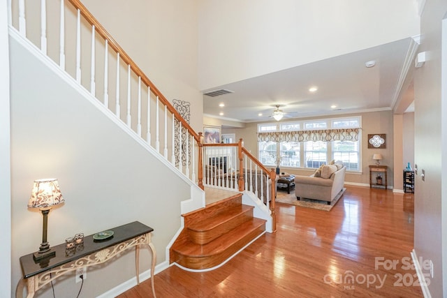 stairs featuring ceiling fan, ornamental molding, and wood-type flooring