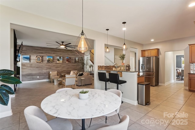 dining area featuring light tile patterned flooring, wood walls, ceiling fan, and sink