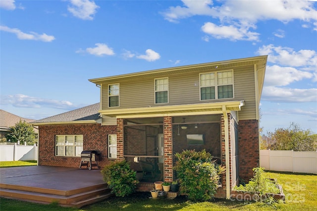 rear view of property featuring a wooden deck, a sunroom, and a lawn