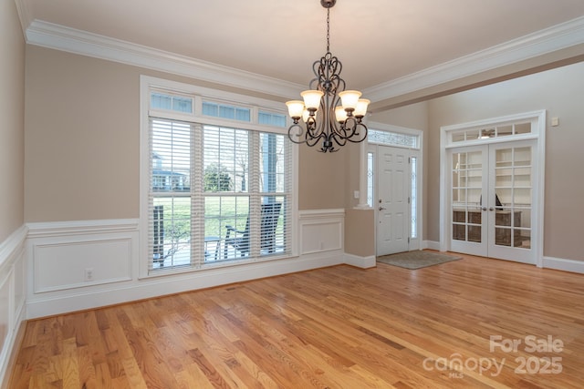 interior space featuring a notable chandelier, light wood-type flooring, crown molding, and french doors