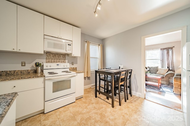 kitchen featuring white cabinetry, dark stone countertops, track lighting, and white appliances