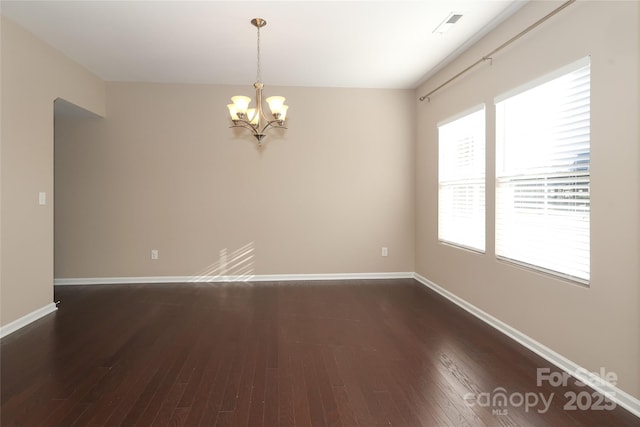 empty room with dark hardwood / wood-style flooring and a notable chandelier